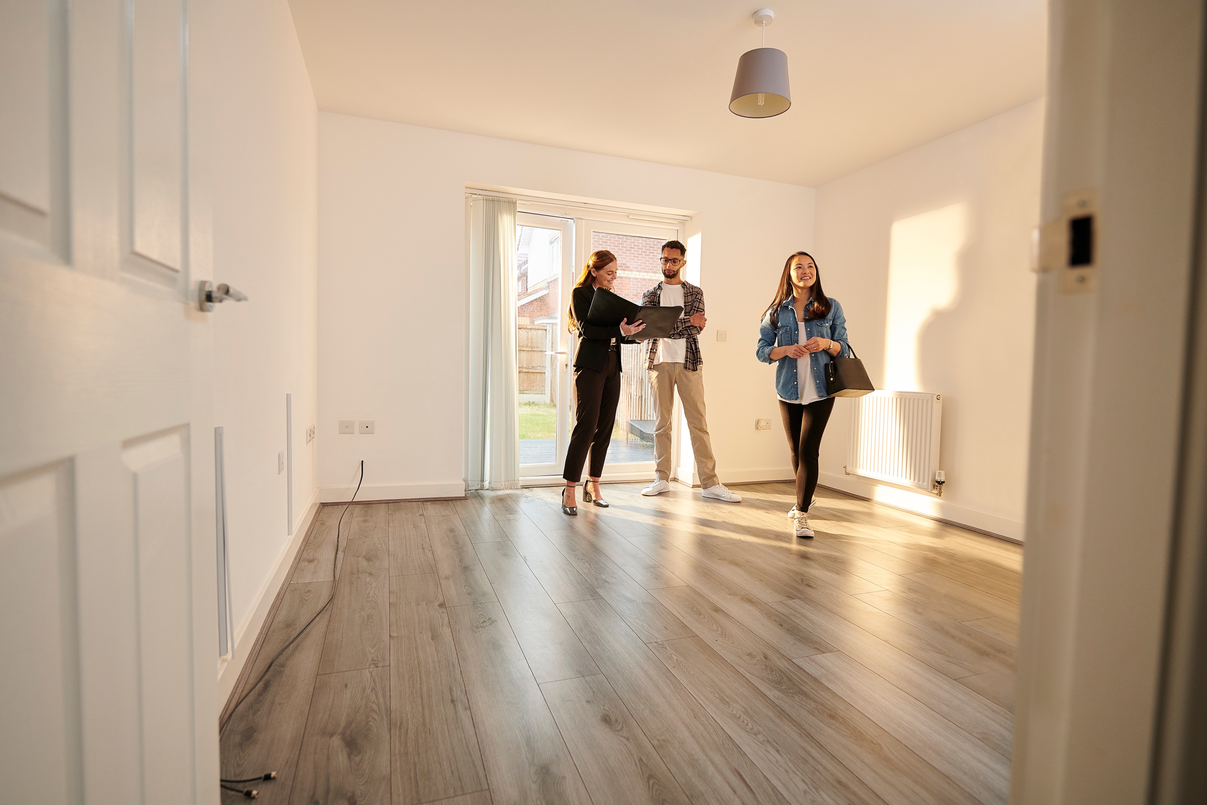 Consultant immobilier indépendant présentant un dossier de vente à des clients lors de la visite d'une maison lumineuse.
