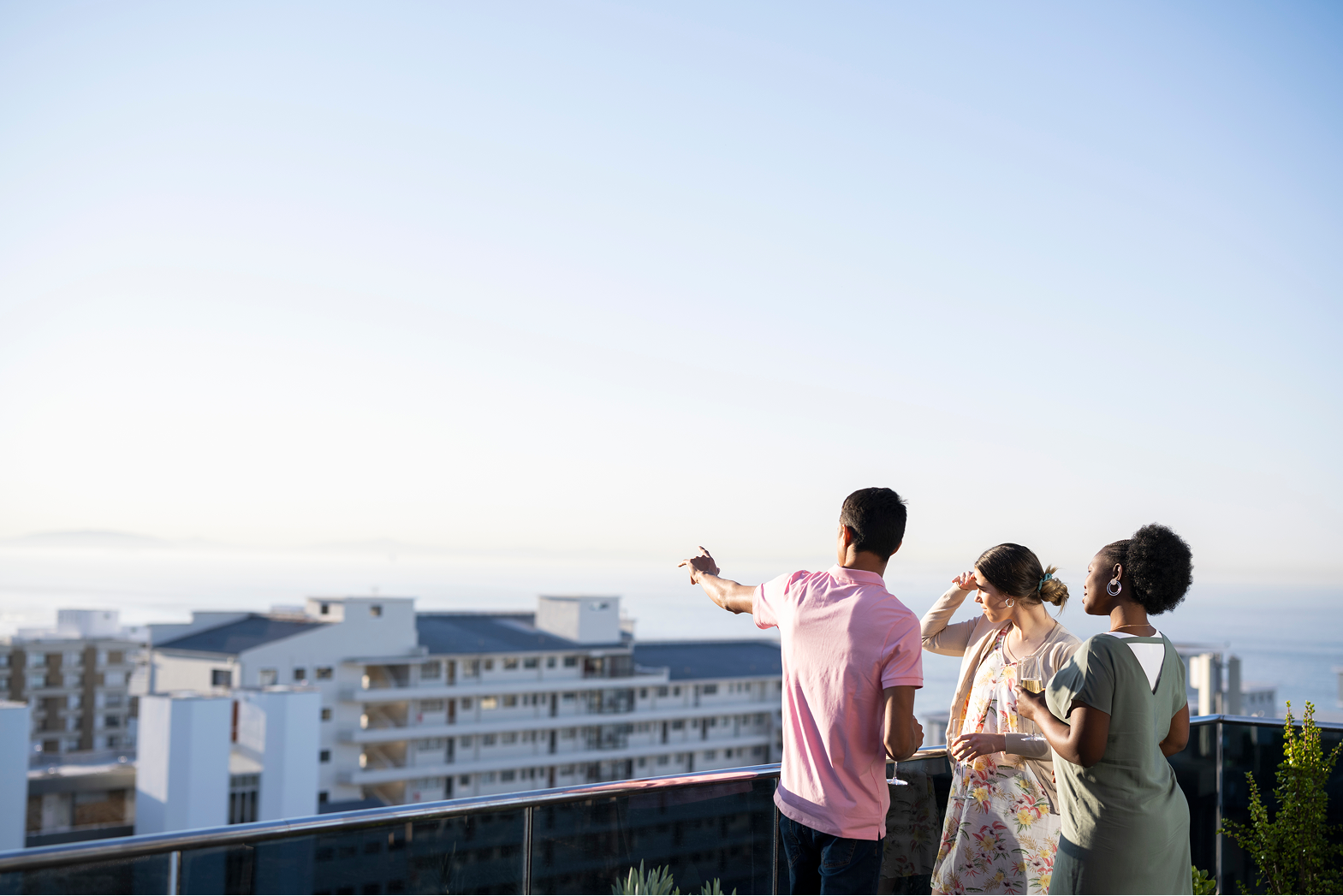 Trois collaborateurs immobiliers discutant sur une terrasse avec vue panoramique sur la ville.